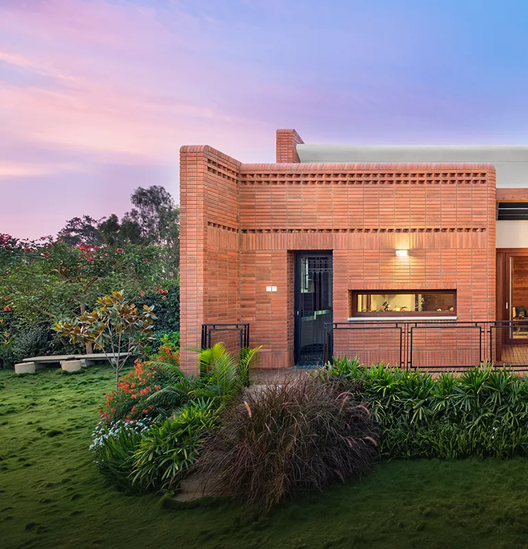 Total Environment After the Rain Brick courtyard villa with lit rooms and a garden at dusk at Total Environment After the Rain
